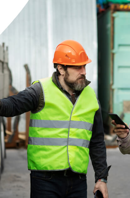Warehouse worker wearing a hard hat and high-visibility vest directing cargo